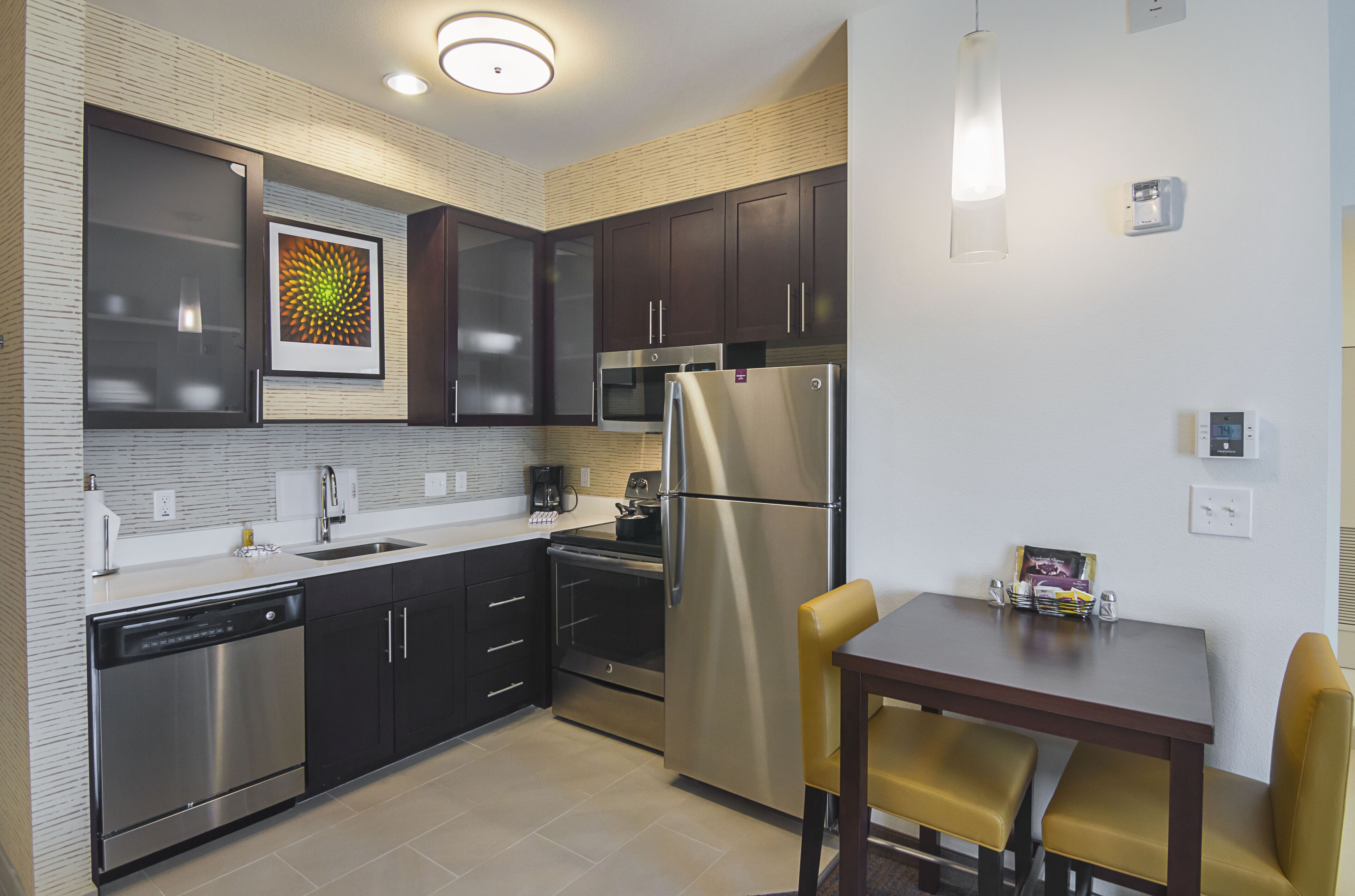 A modern kitchen with stainless steel appliances, dark cabinetry, and a dining area with yellow chairs.