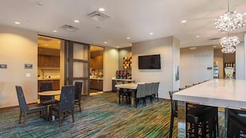 A hotel lobby with a long reception desk, a dining area with a high table and chairs, and a bar area with stools.