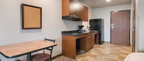 A compact kitchen with a dining table and chairs, a refrigerator, and wooden cabinets.