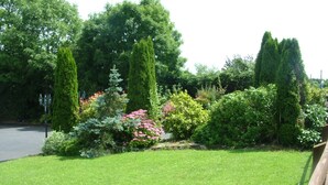 A well-maintained garden with various shrubs and trees, a paved path, and a wooden fence. - Quarry Ridge B&B (Killeshin)