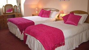 A bedroom with two beds, each with a pink blanket and pillows, a wooden headboard, bedside lamps, and a mirror above the dresser. - Quarry Ridge B&B (Killeshin)