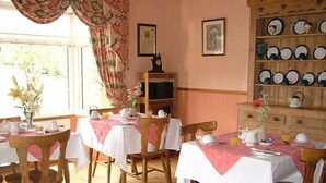 A dining area with wooden chairs and tables, a cabinet with plates, and a window with curtains. - Quarry Ridge B&B (Killeshin)