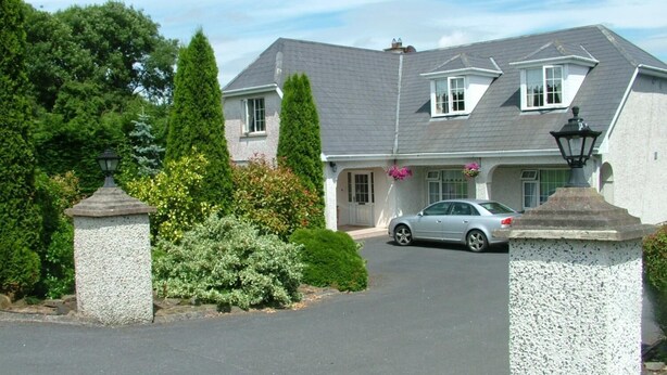 A two-story house with a driveway, a car parked in the driveway, and a well-maintained garden with various plants and shrubs. - Quarry Ridge B&B (Killeshin)