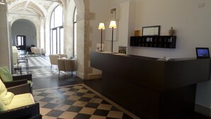 A reception area with a checkered floor, a reception desk, two lamps, a seating area with chairs, and a hallway leading to another room.