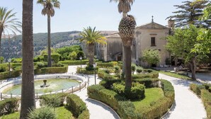 A landscaped garden with palm trees, a fountain, and a building with a cross on top.