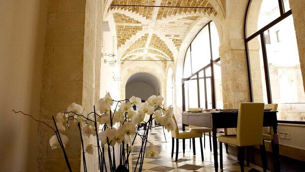 A corridor with arched ceilings and large windows, leading to a dining area with chairs and a table.
