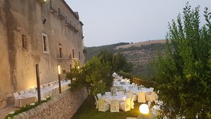 An outdoor dining area with round tables set up along a stone wall, overlooking a hillside.