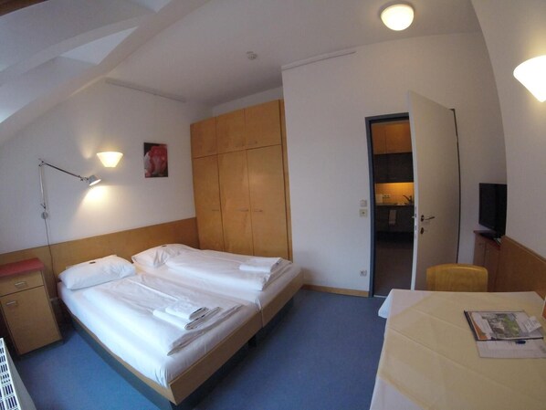 A hotel room with two beds, a desk, a chair, a TV, and a wardrobe.