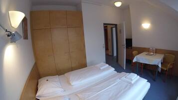 A hotel room with a large bed, a wardrobe, a desk with a chair, and two wall-mounted lamps.