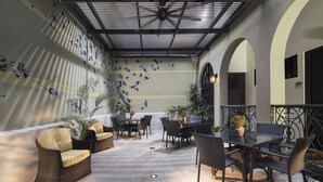 Un patio al aire libre con mobiliario de mimbre, plantas en macetas y una pared decorada con siluetas de pájaros.
