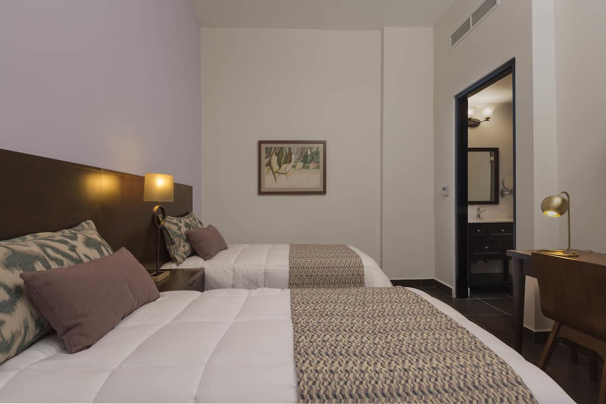 A hotel room with two beds, a desk, a chair, a mirror, and a framed picture on the wall.