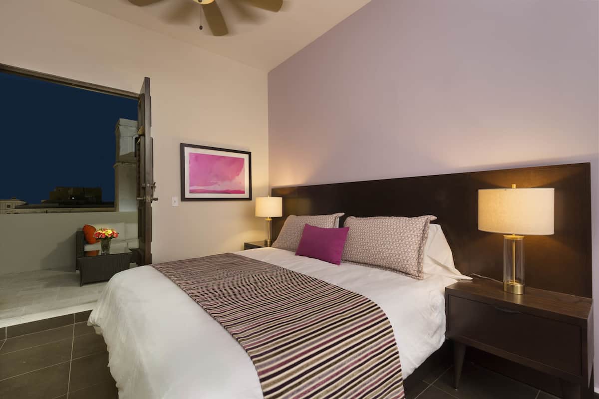 A hotel room with a bed, two bedside tables, a nightstand, a window, and a ceiling fan.
