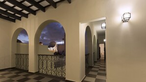 Un pasillo con suelo a cuadros, arcos y vista al cielo.