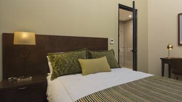 A hotel room with a bed, a bedside table with a lamp, a nightstand, and a mirror on the wall.