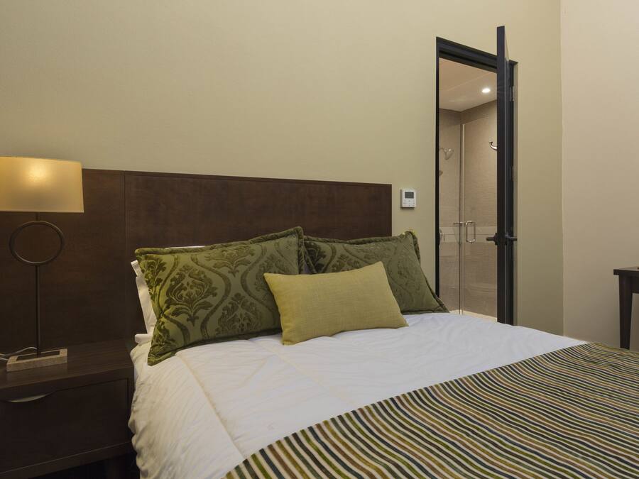 Une chambre d’hôtel avec un lit, une table de chevet avec une lampe, une commode et un miroir au mur.