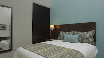 A neatly made bed with patterned bedding, a bedside lamp, and a mirror on the wall.