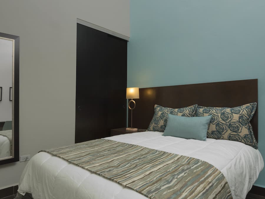 A neatly made bed with patterned bedding, a bedside lamp, and a mirror on the wall.