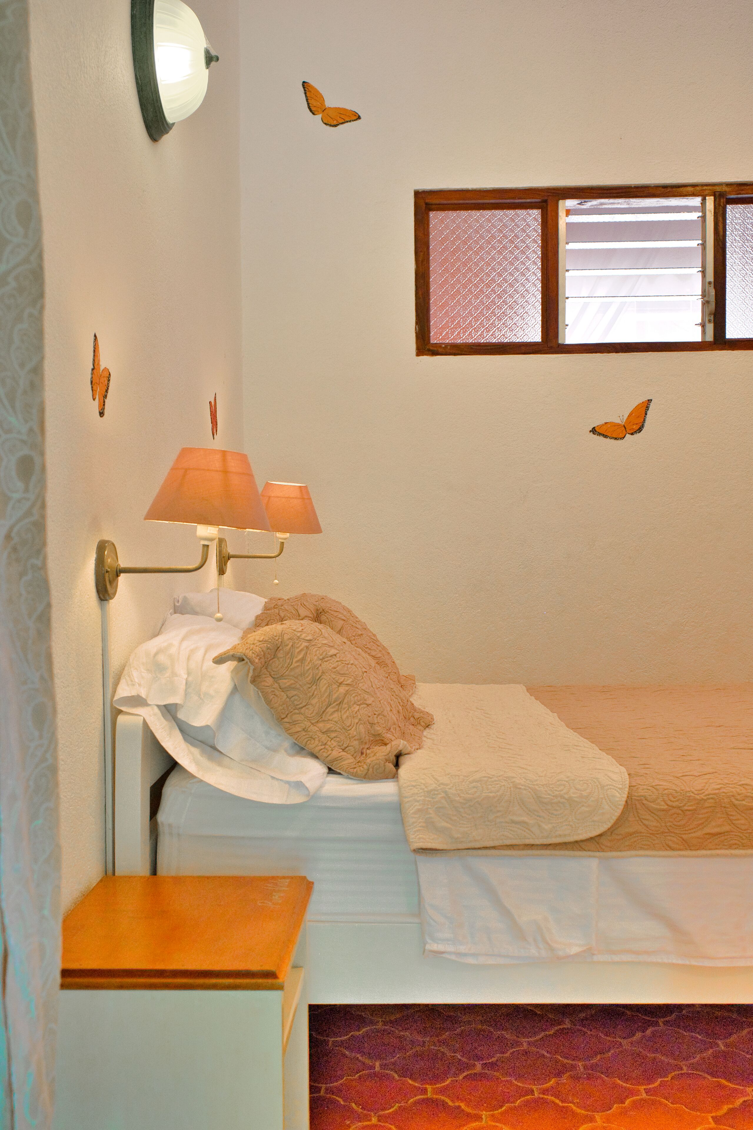 A bedroom with a bed, a nightstand, a wall-mounted lamp, and butterfly decals.