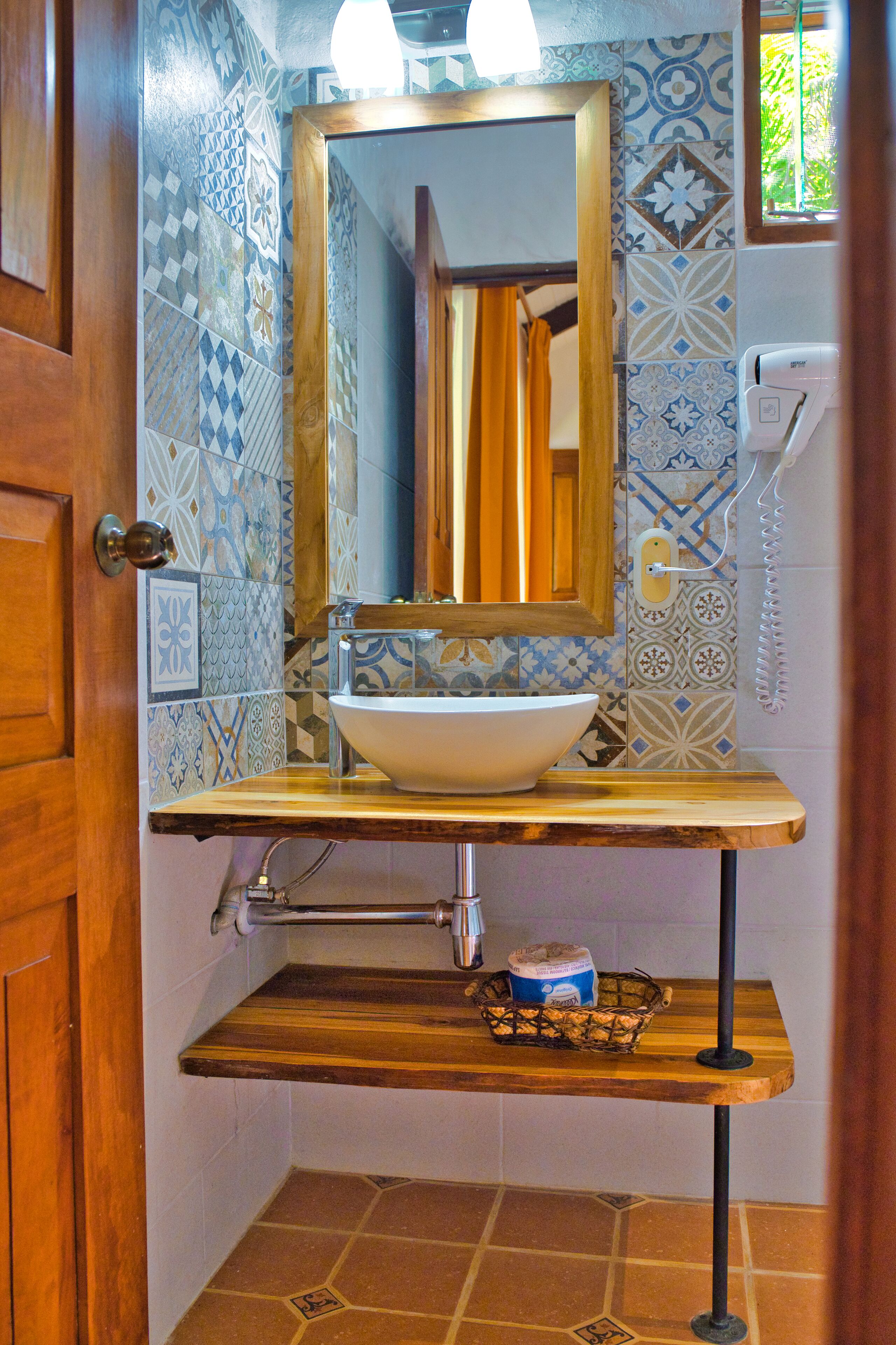 Un baño con lavamanos blanco, encimera de madera y azulejos estampados.