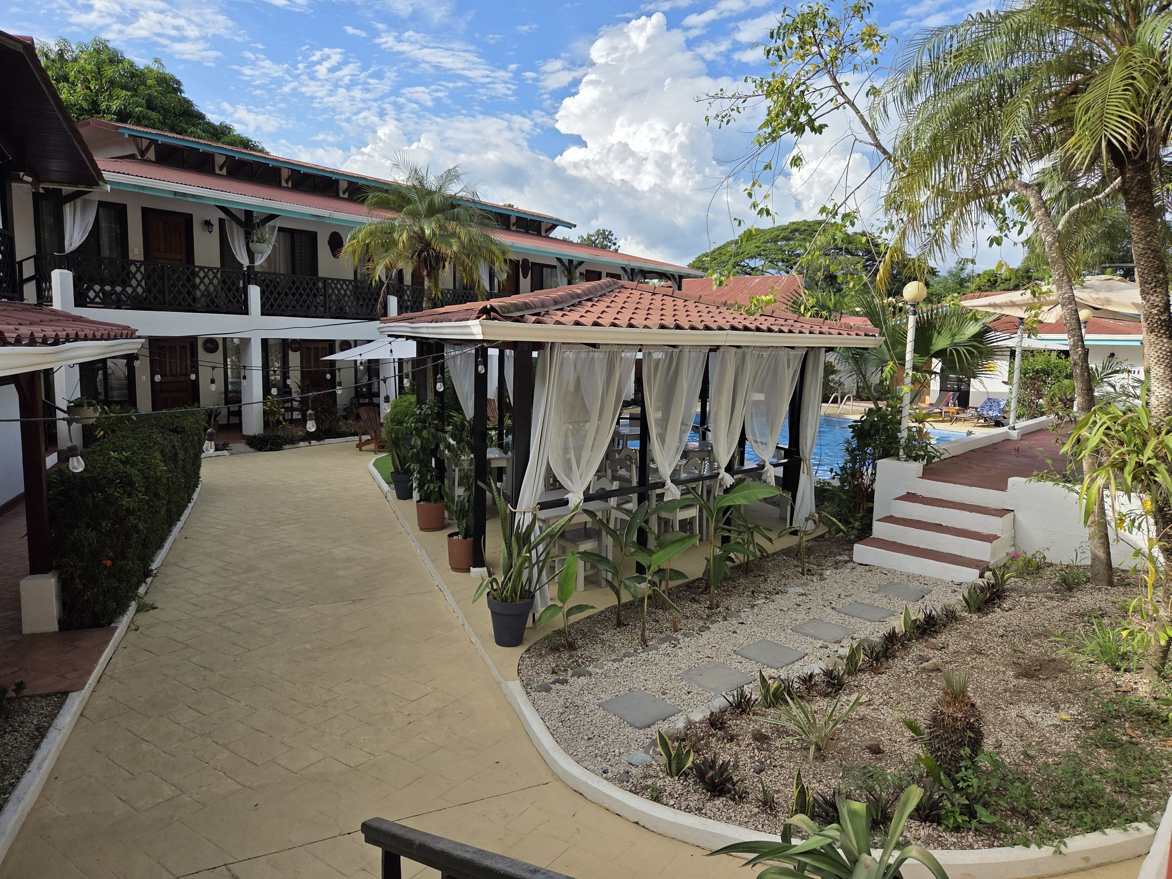 A hotel courtyard with a pool, covered seating areas, and potted plants.