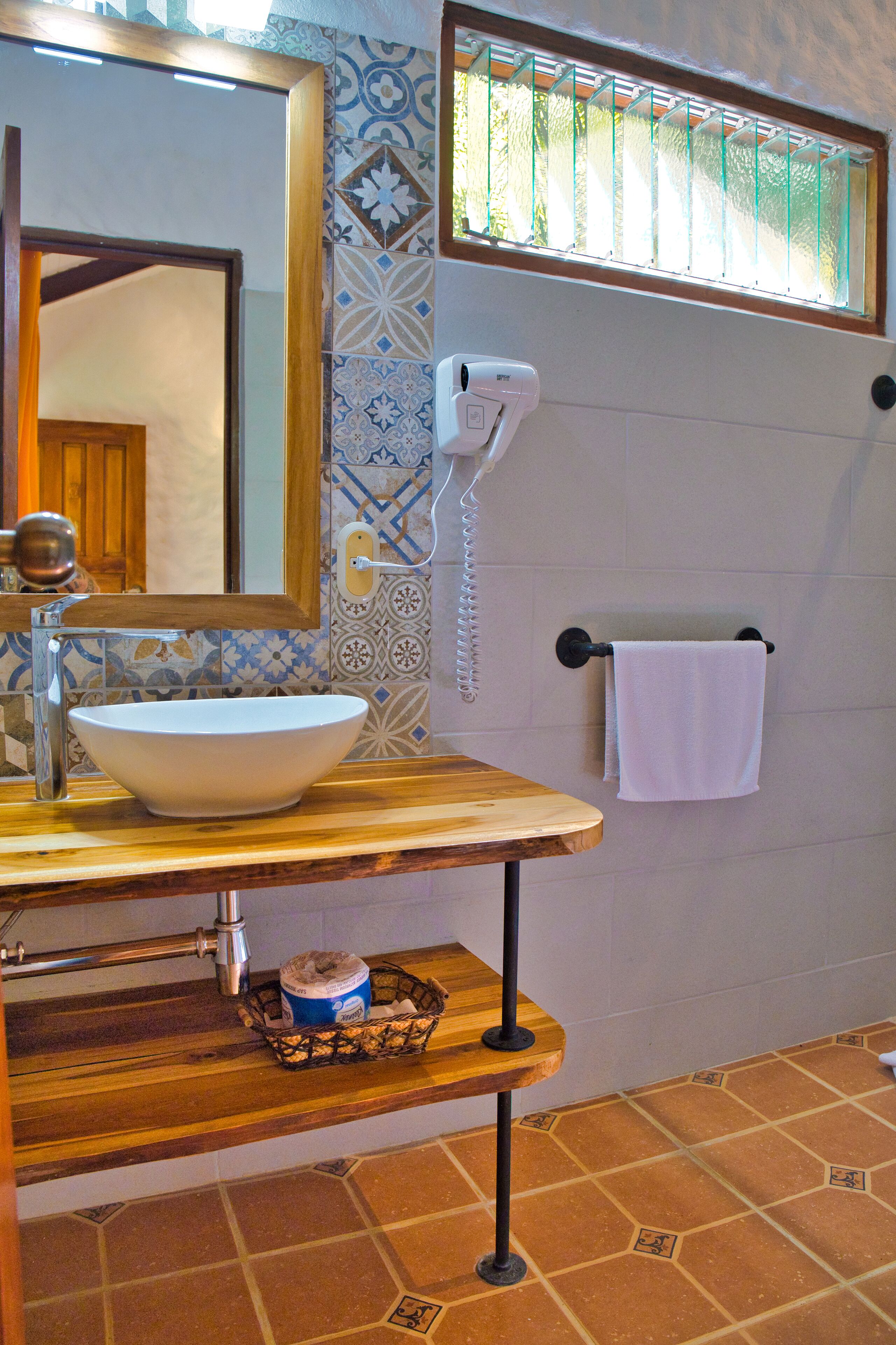 A bathroom with a white sink, a wooden vanity, a mirror, a towel rack, and patterned tiles.