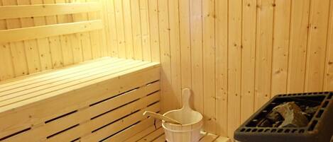 A sauna with wooden benches, a white bucket, and a sauna heater.