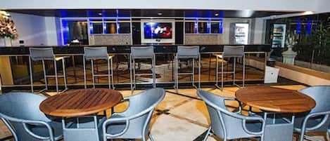 Zona de bar con mesas y sillas redondas, una pantalla de televisión y una decoración interior moderna.