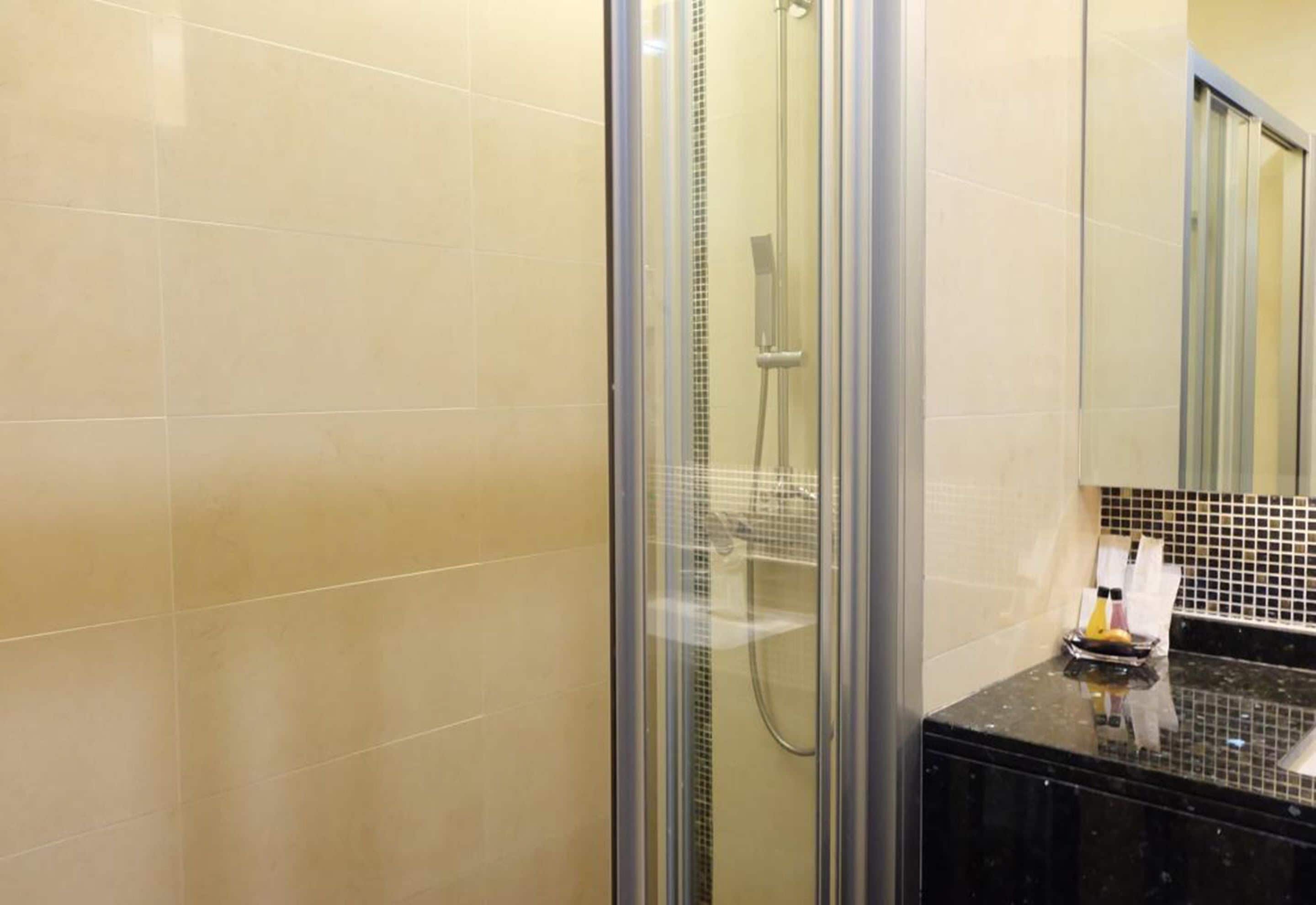 Un baño con ducha envuelta en vidrio, azulejos color beige y un mostrador negro con dispensador de jabón.