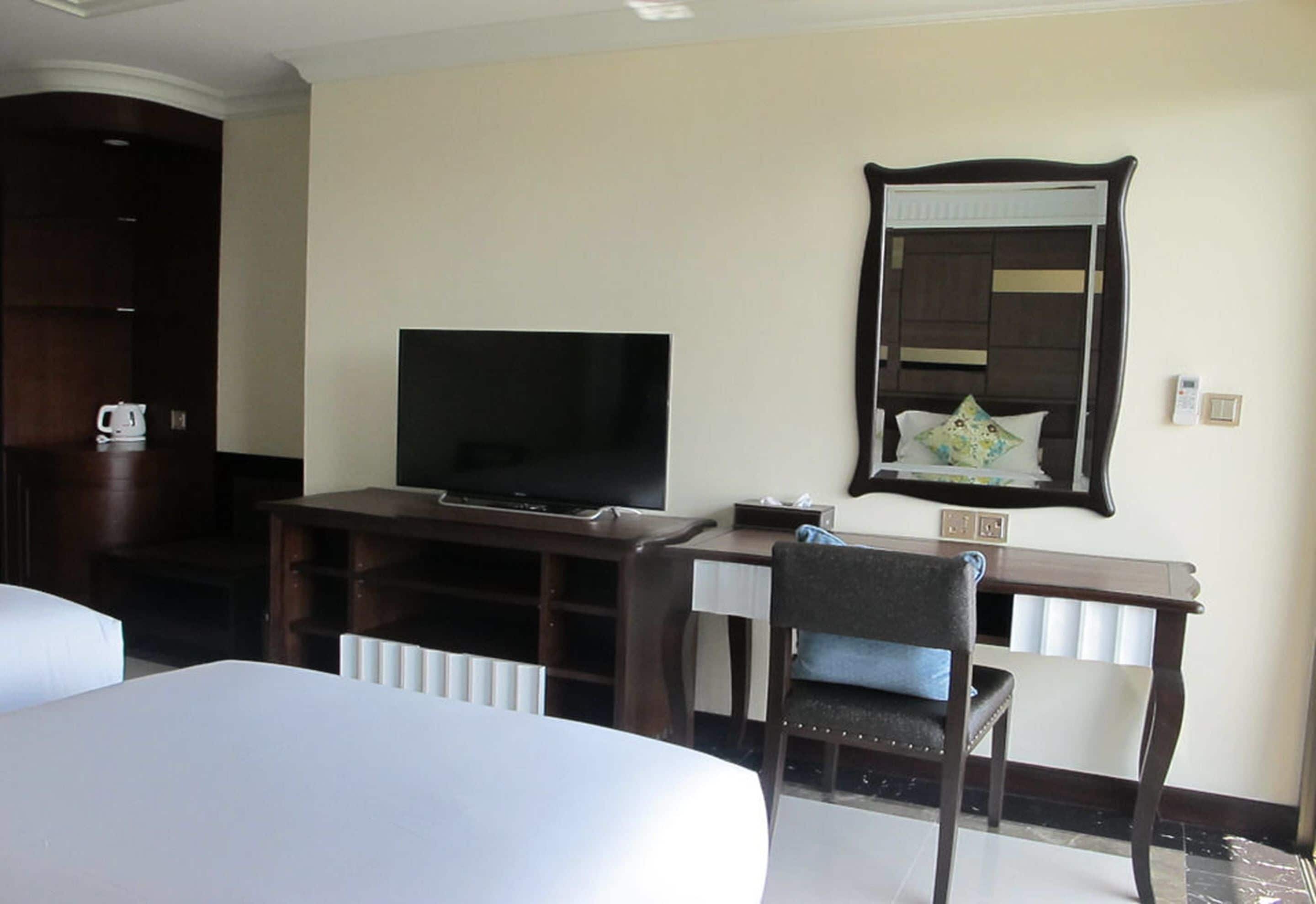 A hotel room with a bed, a desk with a television, a chair, and a mirror on the wall.