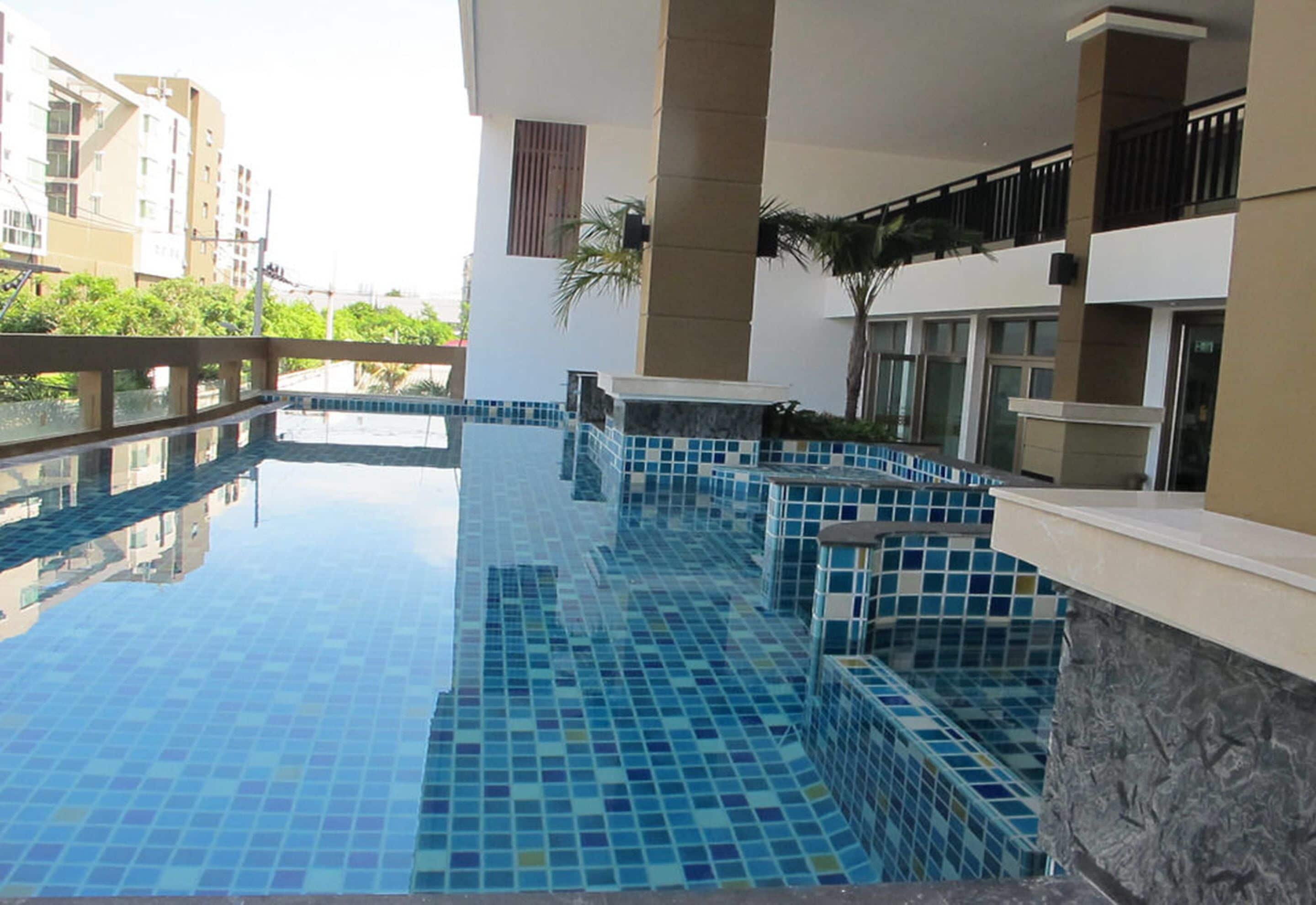 A swimming pool with blue tiles, surrounded by a stone wall and a balcony with a railing.