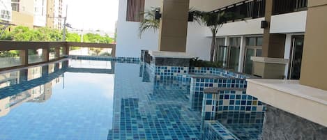 A swimming pool with blue tiles, surrounded by a stone wall and a balcony with a railing.