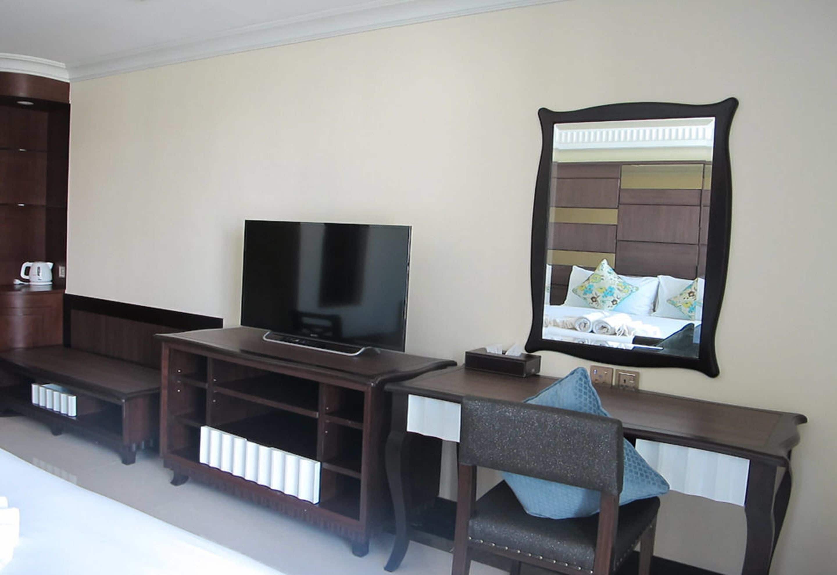 Habitación de hotel con televisión sobre un soporte de madera, un espejo y una cama con almohada azul.
