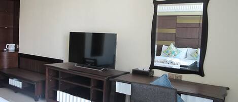 Habitación de hotel con televisión sobre un soporte de madera, un espejo y una cama con almohada azul.