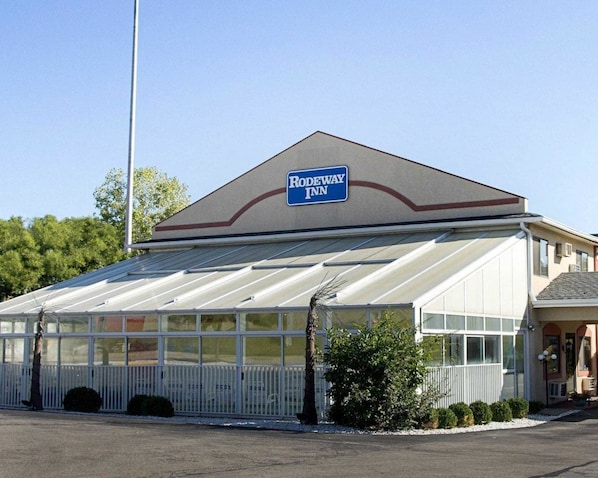 A building with a sign reading "Rodeway Inn." It features a large glass enclosure, a white fence, and a clear sky.