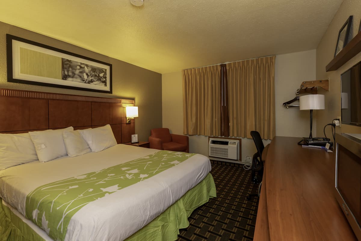 A hotel room with a large bed, a desk with a computer, a chair, an air conditioning unit, and a lamp.