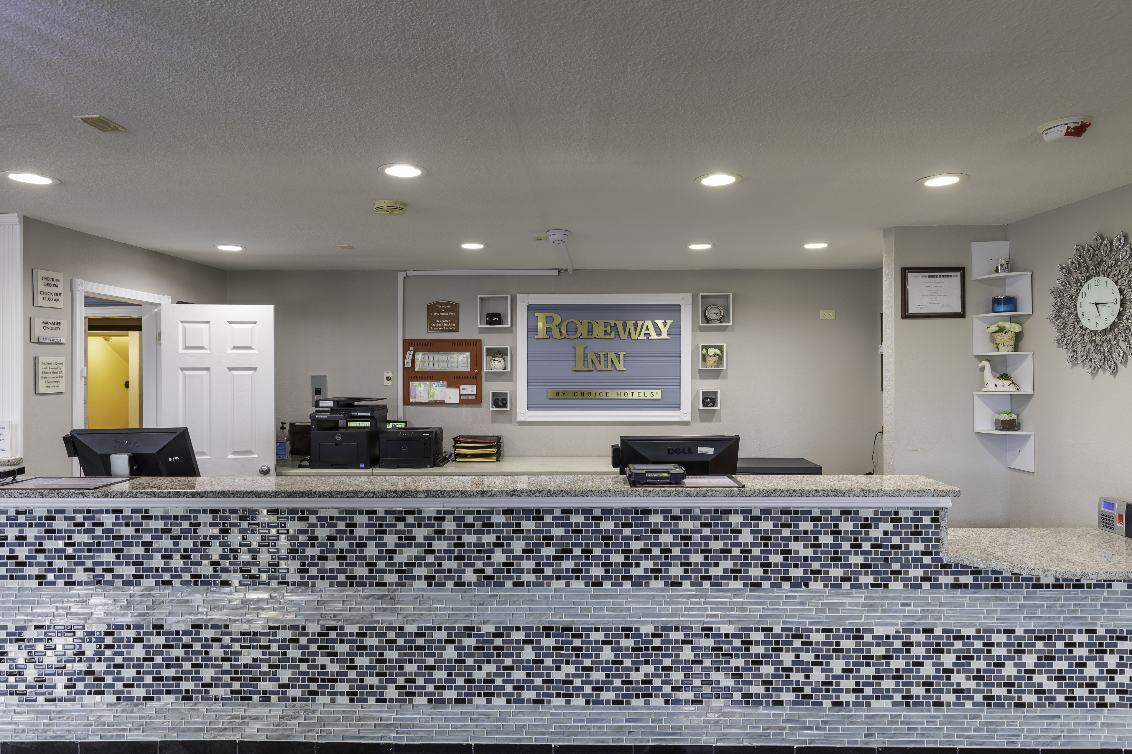 Un área de recepción con mostrador de mosaicos, un letrero de Rodeway Inn y varios objetos enmarcados en la pared.