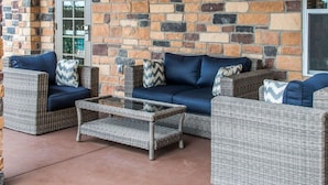 A covered outdoor seating area with wicker furniture and a stone wall backdrop. - MainStay Suites Cotulla (Cotulla)