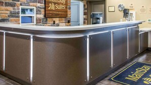 A hotel reception area with a stone wall, a MainStay Suites sign, a coffee machine, and a digital clock. - MainStay Suites Cotulla (Cotulla)
