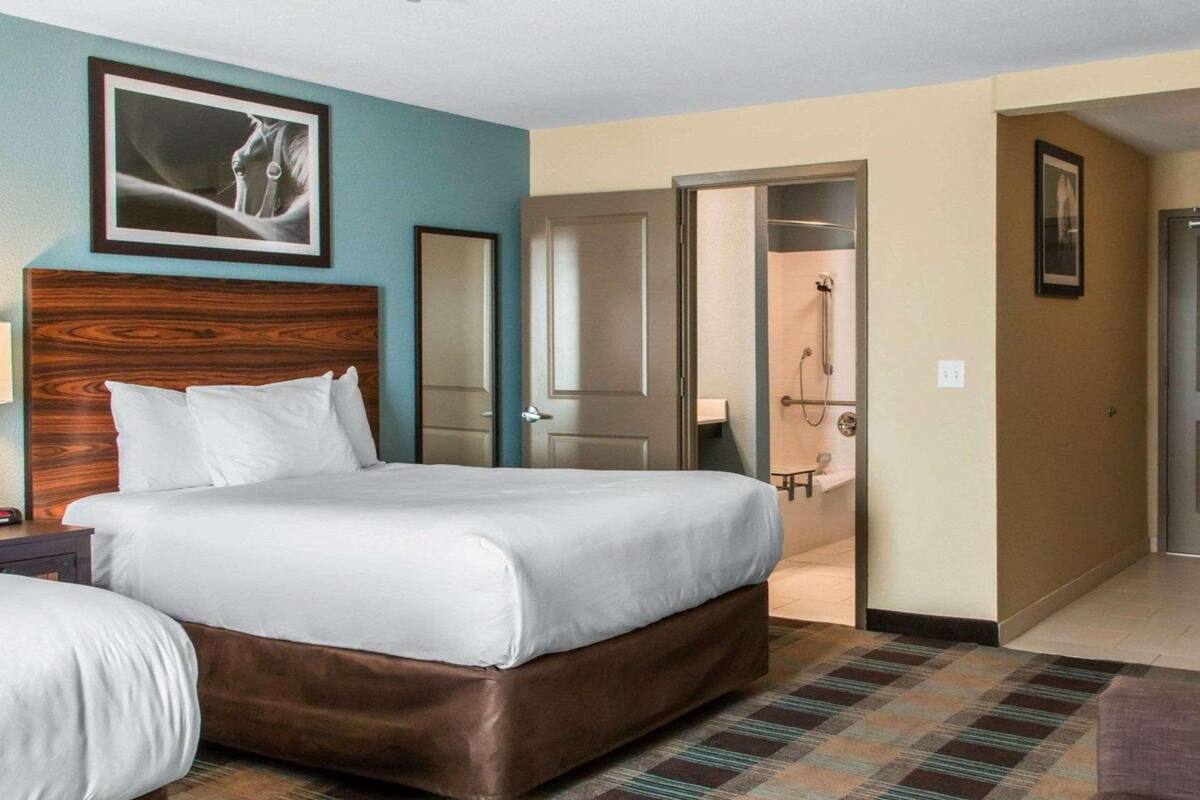 Ein Hotelzimmer mit einem großen Bett, einem kleineren Bett, einem Holzkopfende, einem Schachbrettfußboden und einem durchgegangenen Tür angedeuteten Badezimmer.