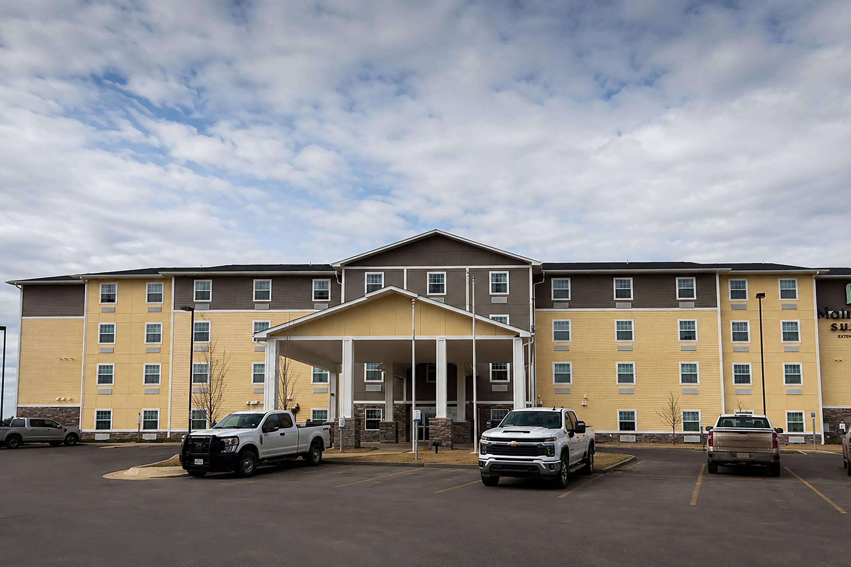 A multi-story hotel with a covered entrance, parking lot, and several vehicles parked in front.