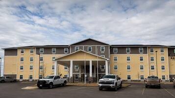 A multi-story hotel with a covered entrance, parking lot, and several vehicles parked in front.