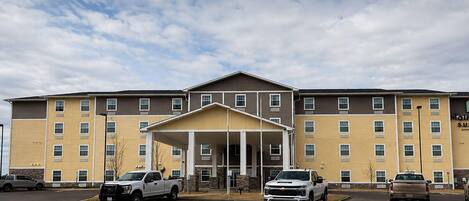 A multi-story hotel with a covered entrance, parking lot, and several vehicles parked in front.