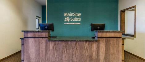 A reception desk with a teal wall and a sign that reads "MainStay Suites by Choice Hotels".