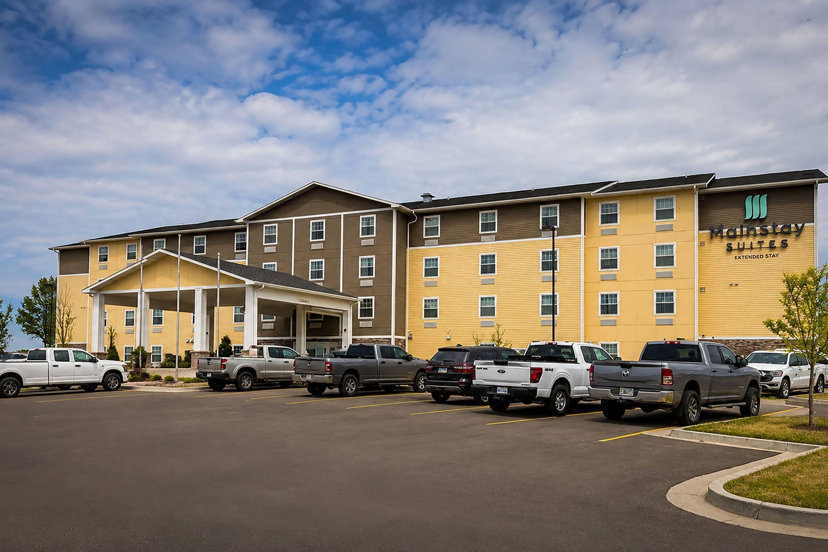 Ein Hotel mit Parkplatz, mehreren Fahrzeugen und einem Gebäude mit der Aufschrift 'Mainstay Suites Extended Stay'.