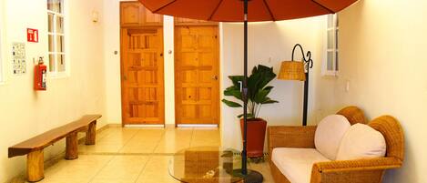 A lobby with a bench, a glass-top table, a wicker sofa, a potted plant, and a large umbrella.