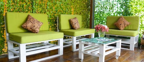A seating area with three green cushioned sofas and a glass coffee table, set against a wall covered with green foliage.