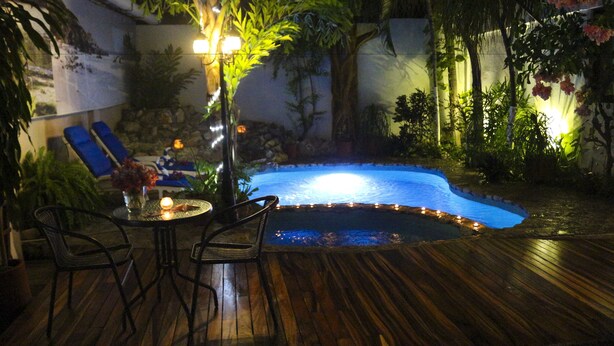 An outdoor pool area with a wooden deck, lounge chairs, and a table with candles. - Hotel Careyes Puerto Escondido (Puerto Escondido)