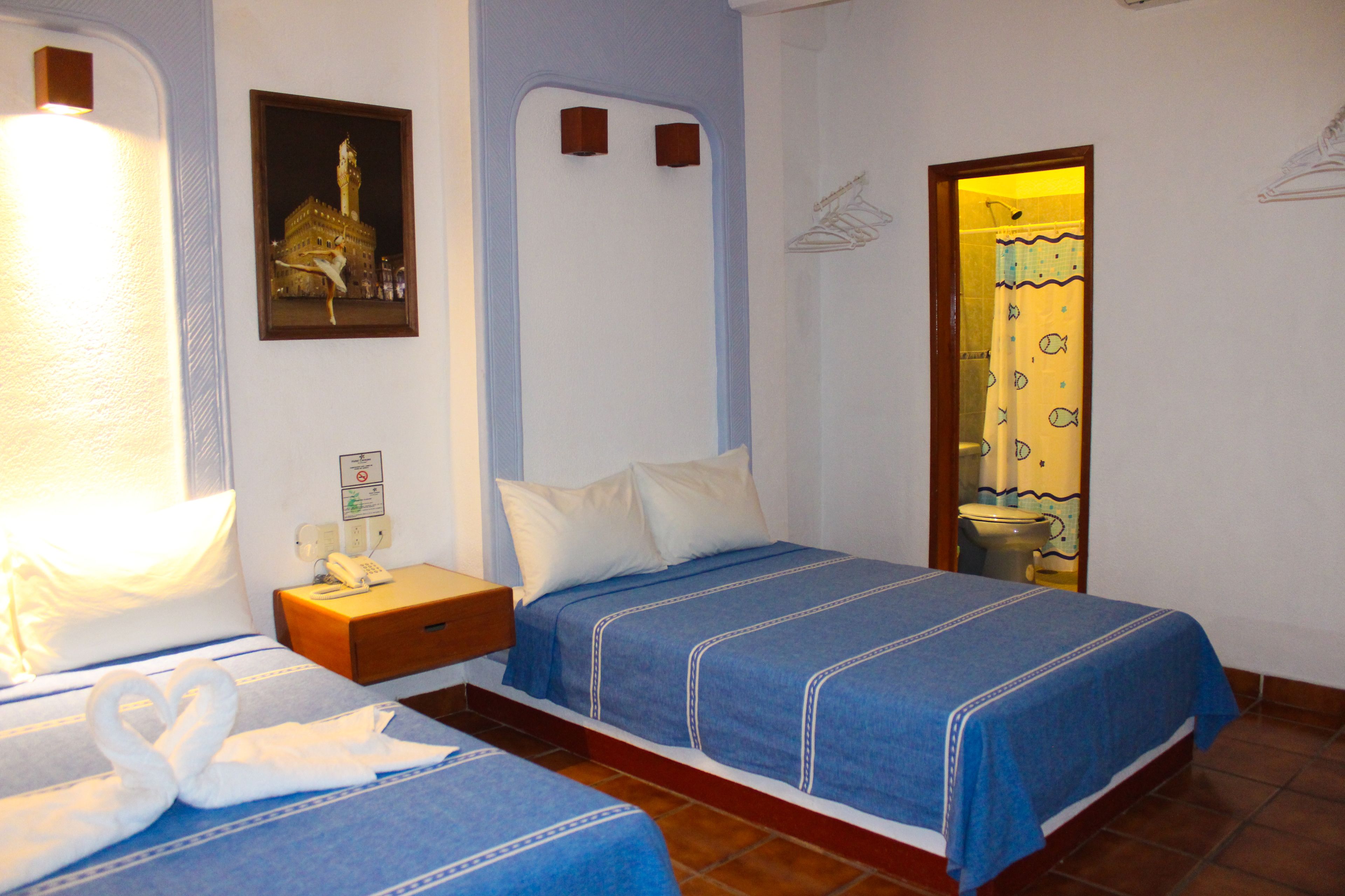Une chambre d’hôtel avec deux lits, une table de chevet, un téléphone fixé au mur et un tableau encadré.