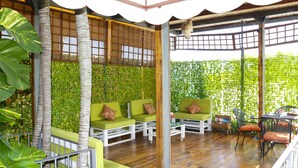 A covered outdoor seating area with green cushioned sofas and chairs, wooden flooring, and a backdrop of green foliage. - Hotel Careyes Puerto Escondido (Puerto Escondido)