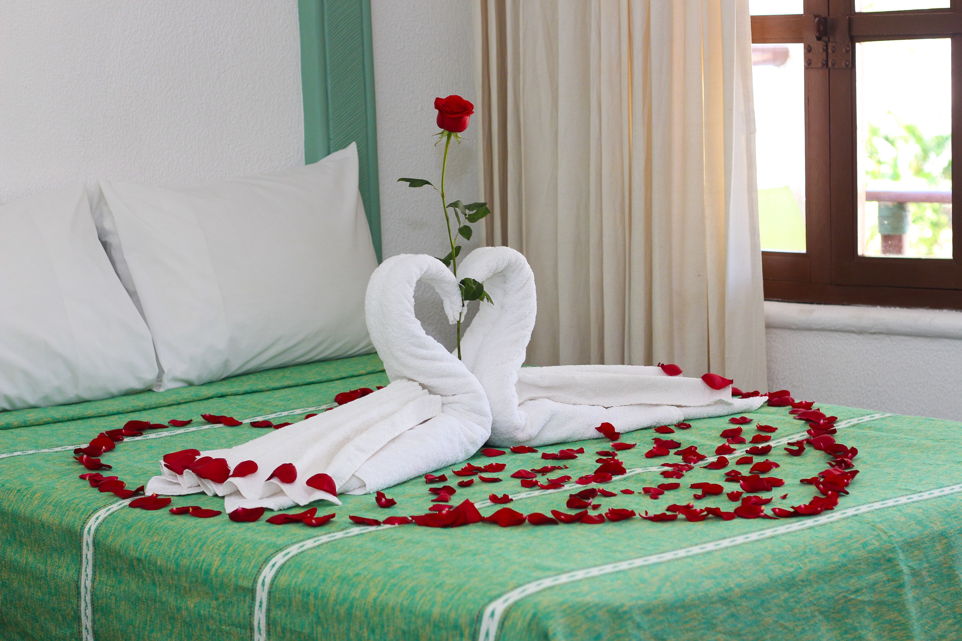 A bed with a green bedspread, white pillows, and a rose.